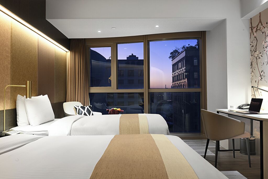 Habitación de hotel con una cama grande, un escritorio y vistas a edificios a través de la ventana.