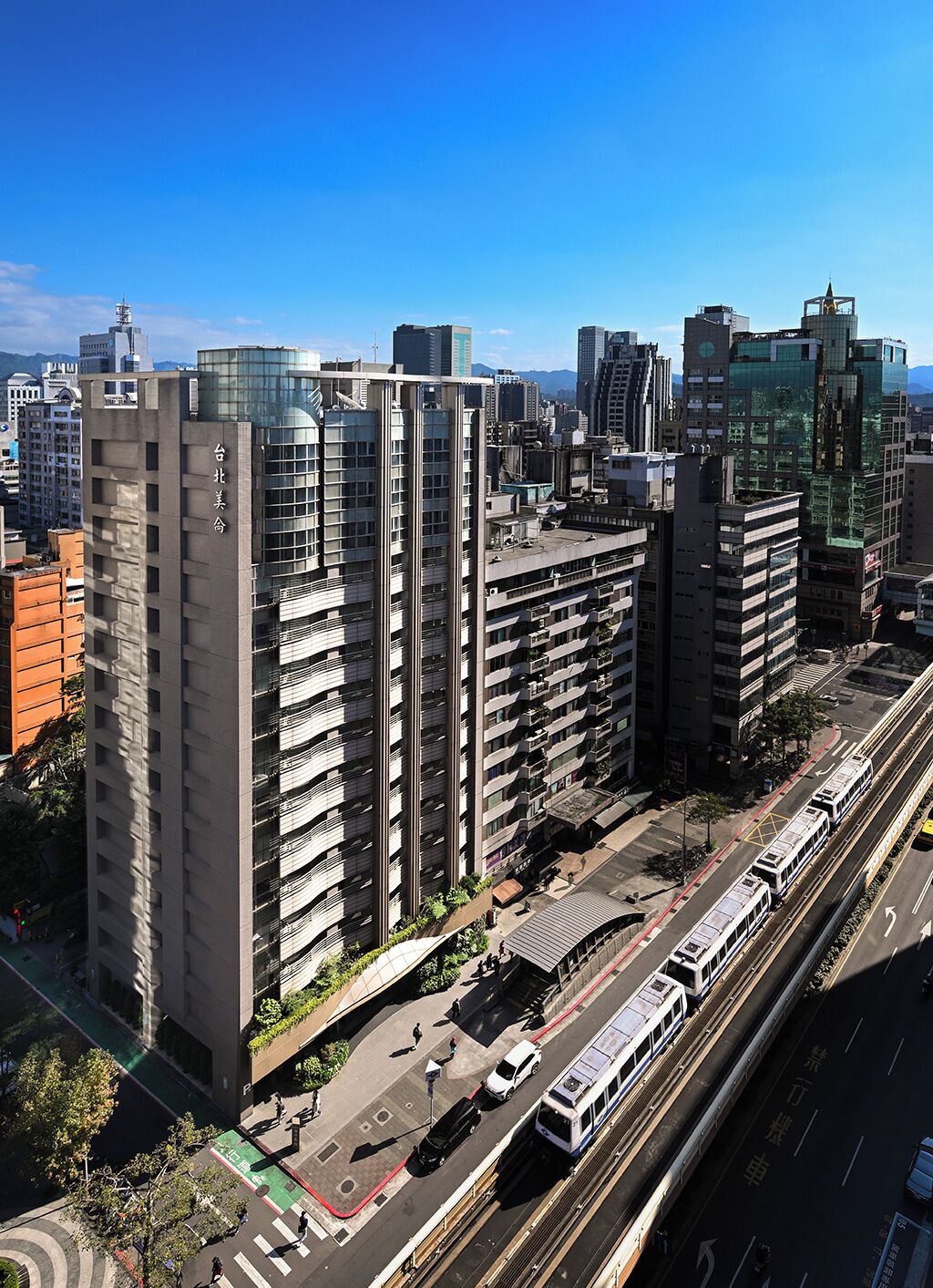 Un edificio de gran altura con varios pisos, un diseño arquitectónico moderno y un paseo peatonal a nivel de calle.