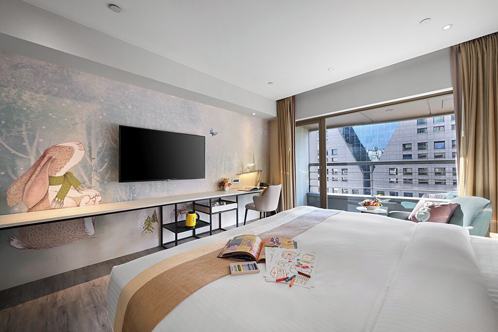 A modern hotel room with a large bed, a desk, a flat-screen TV, and a large window offering a city view.