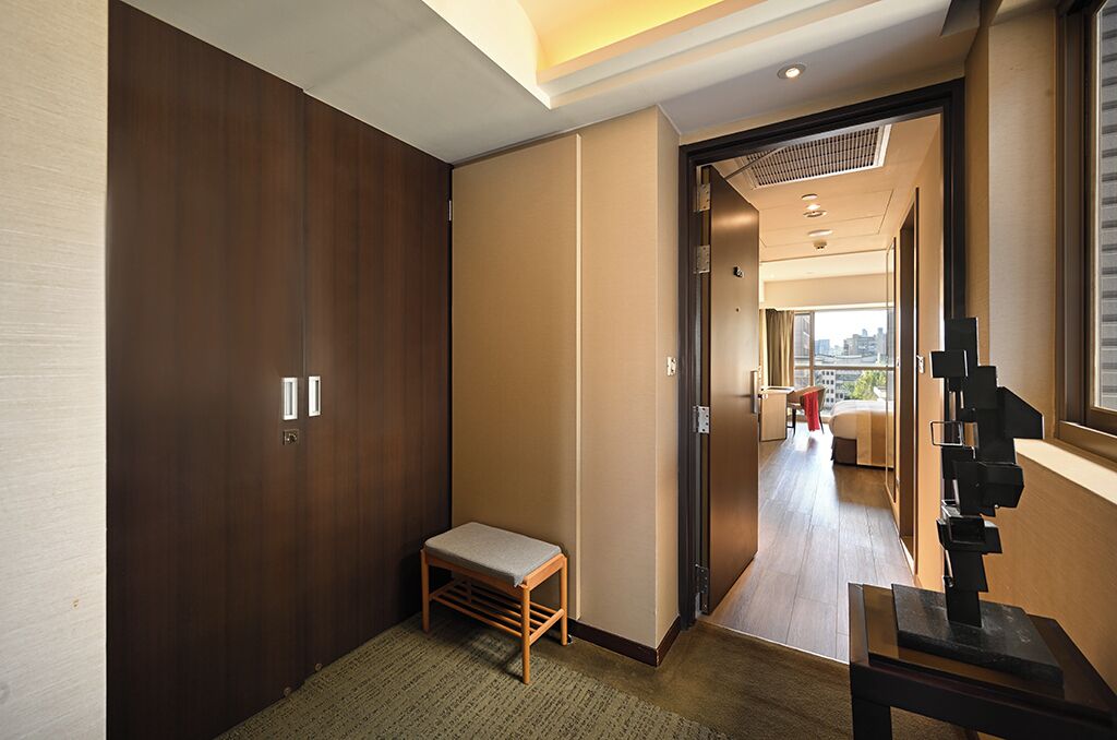 Un pasillo de hotel con un armario de madera, un pequeño banco y una escultura de arte moderno.