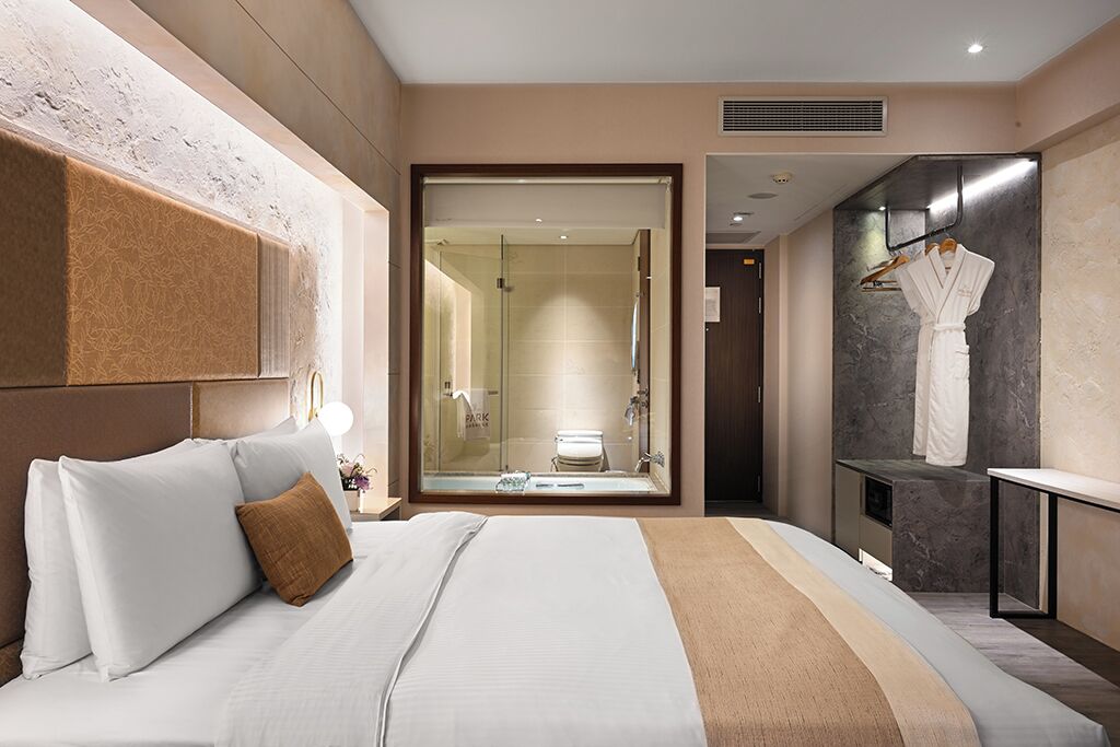 Ein modernes Hotelzimmer mit einem großen Bett, einer Dusche mit Glaswand und einem Bademantel, der an der Wand hängt.