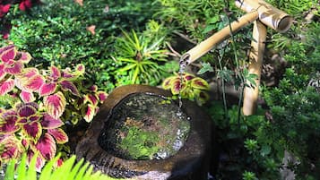 Ein traditioneller Steinbrunnen mit einem Bambus-Auslauf, umgeben von üppigem Grün und geflecktem Laub.
