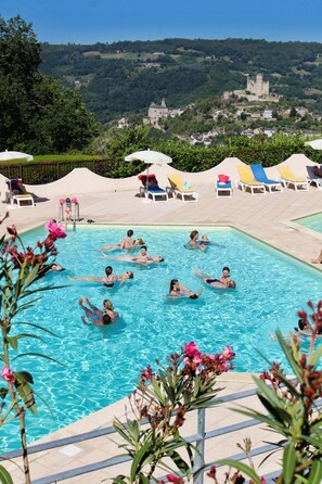 Una piscina con gente nadando, rodeada de sillas de descanso y vistas a un castillo en una colina.