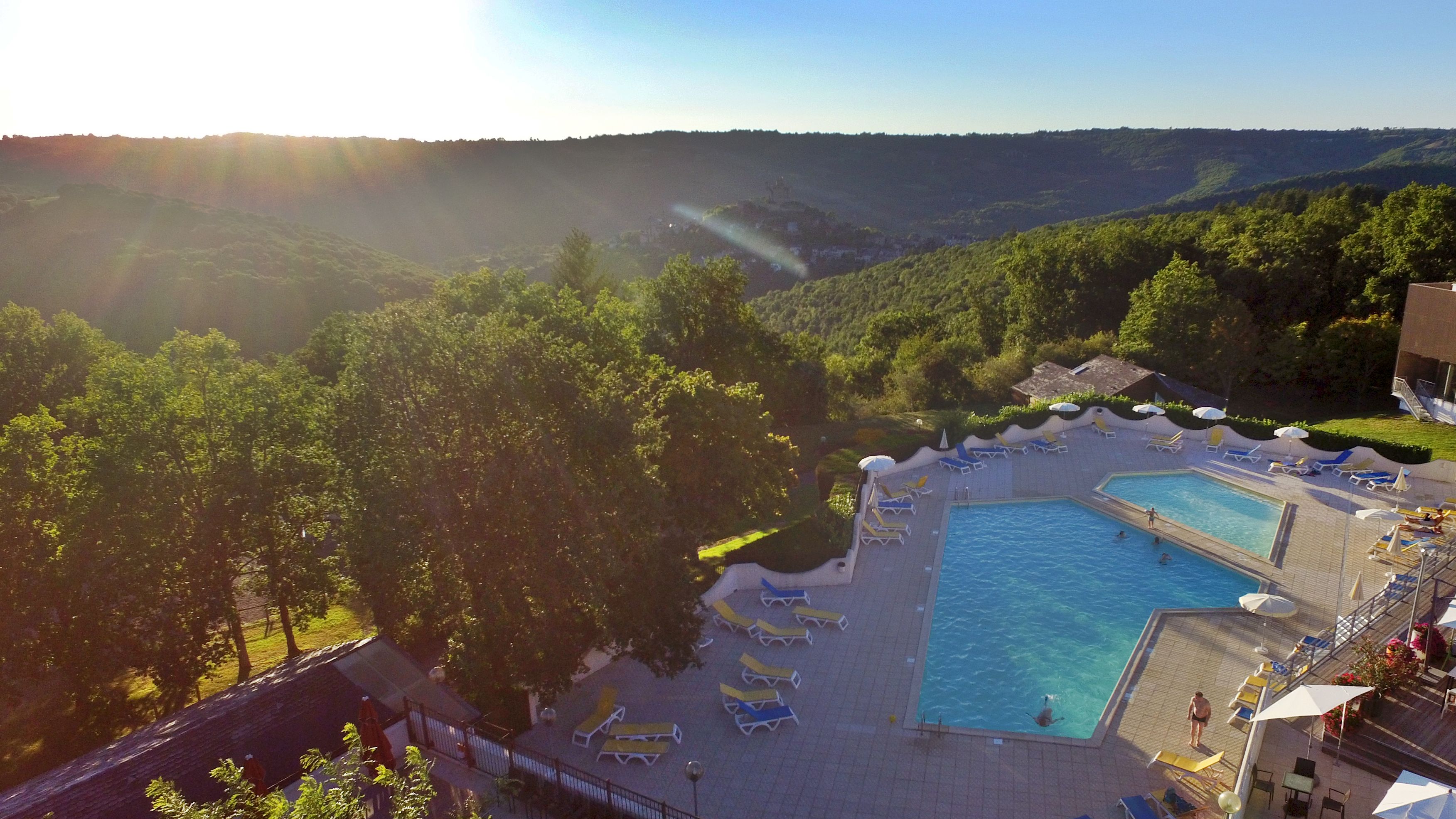 A resort with a swimming pool, sun loungers, and a view of the surrounding hills.