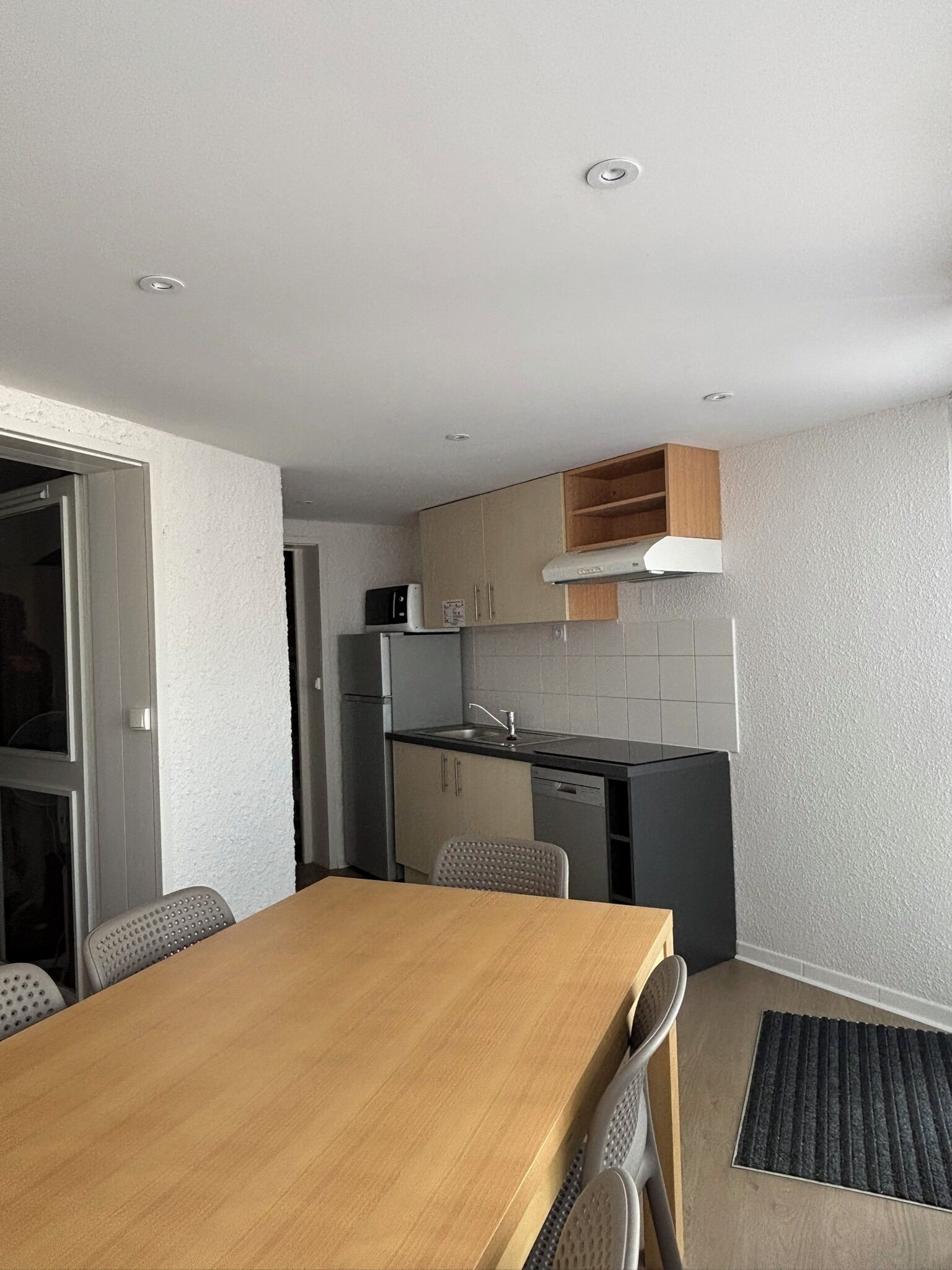 A compact kitchen with a dining area, including a wooden table and chairs, a built-in oven, and a microwave.