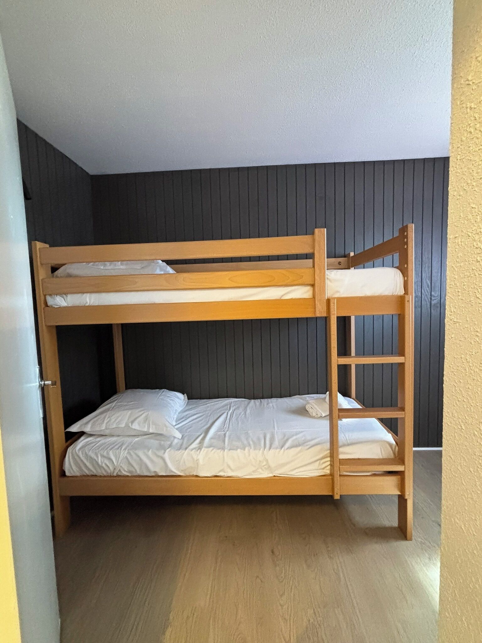 Un lit superposé à deux niveaux, avec une structure en bois et une literie blanche.