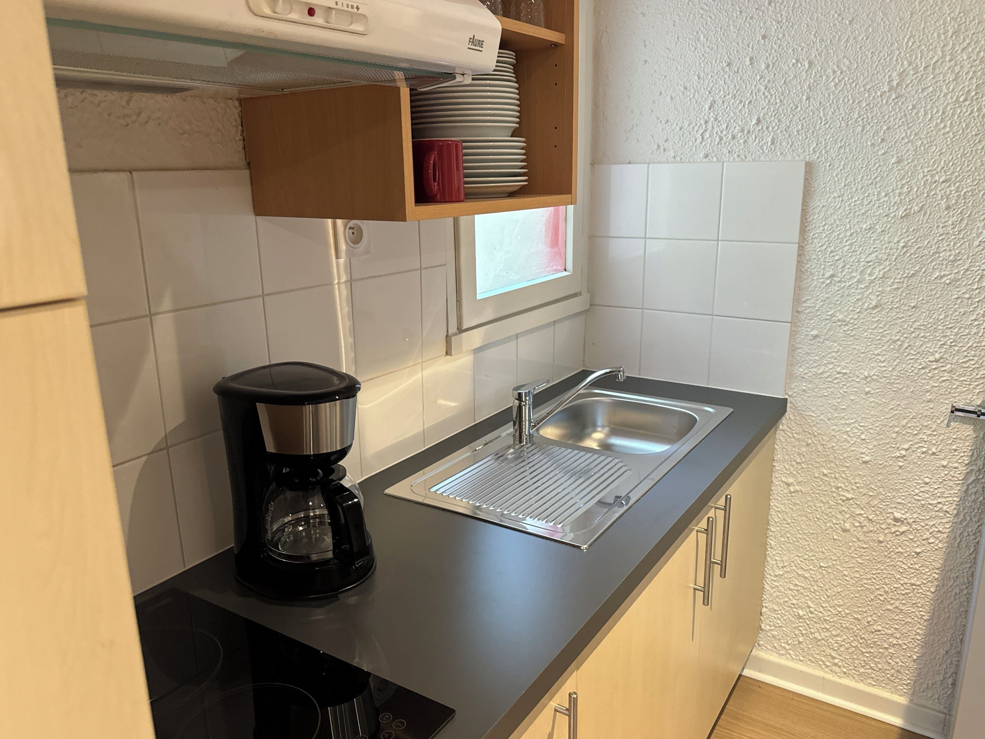 A compact kitchen with a built-in coffee maker, a sink, and a window.