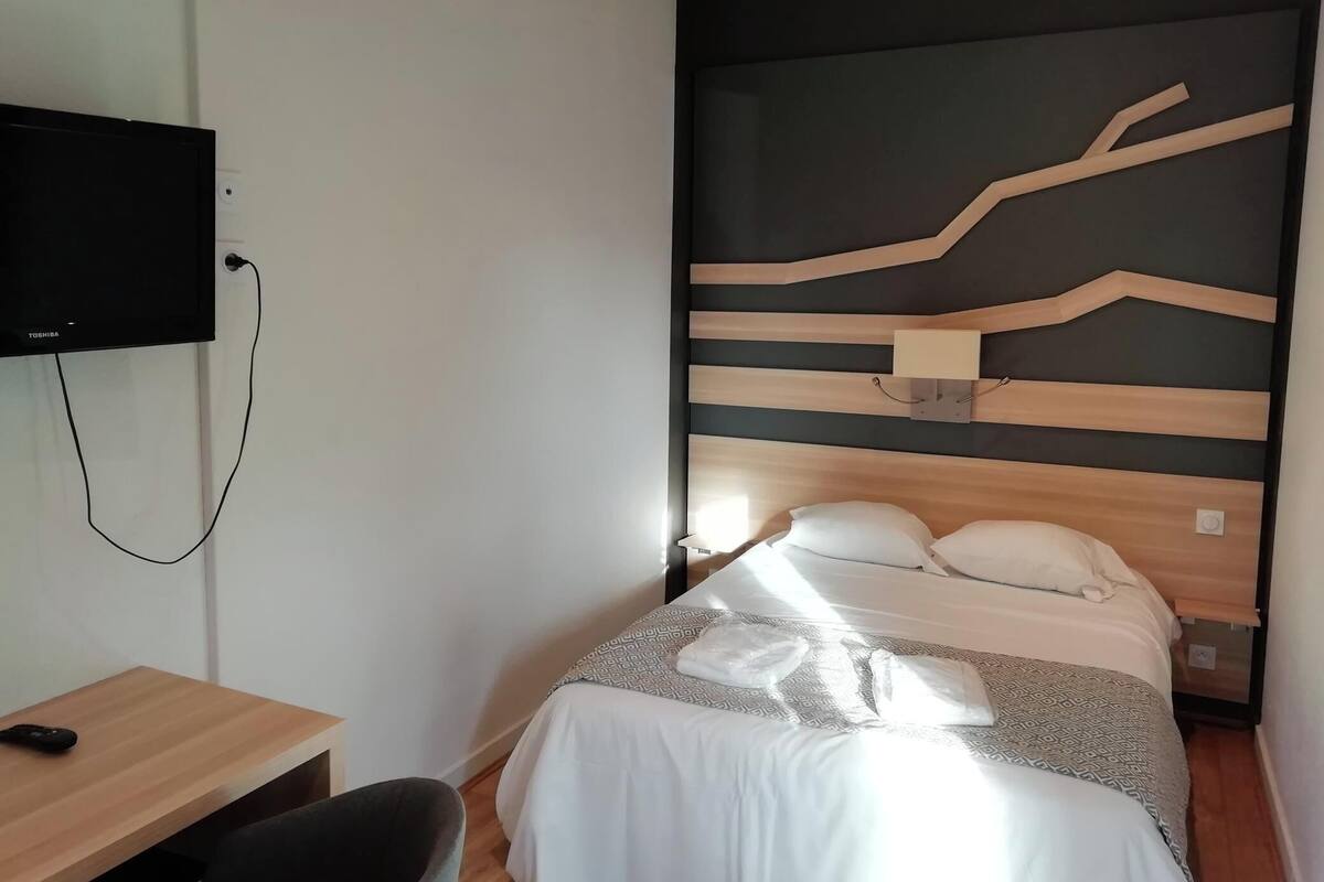 A hotel room with a bed, a desk, a TV mounted on the wall, and a modern wall design.