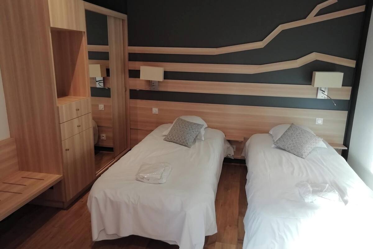 A hotel room with two single beds, wooden wardrobe, and a modern wall design.
