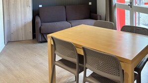 A modern room with a wooden floor, a grey sofa, a wooden table with chairs, and a ceiling light fixture.