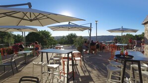 An outdoor patio with tables and chairs, umbrellas, and a view of the landscape.