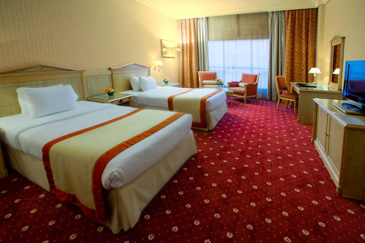 Habitación de hotel con dos camas, un escritorio, una silla, un televisor y una ventana con cortinas.