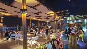 An outdoor dining area with tables and chairs, a pergola structure, and a view of the city skyline at night. - Capitol Hotel (Dubai)