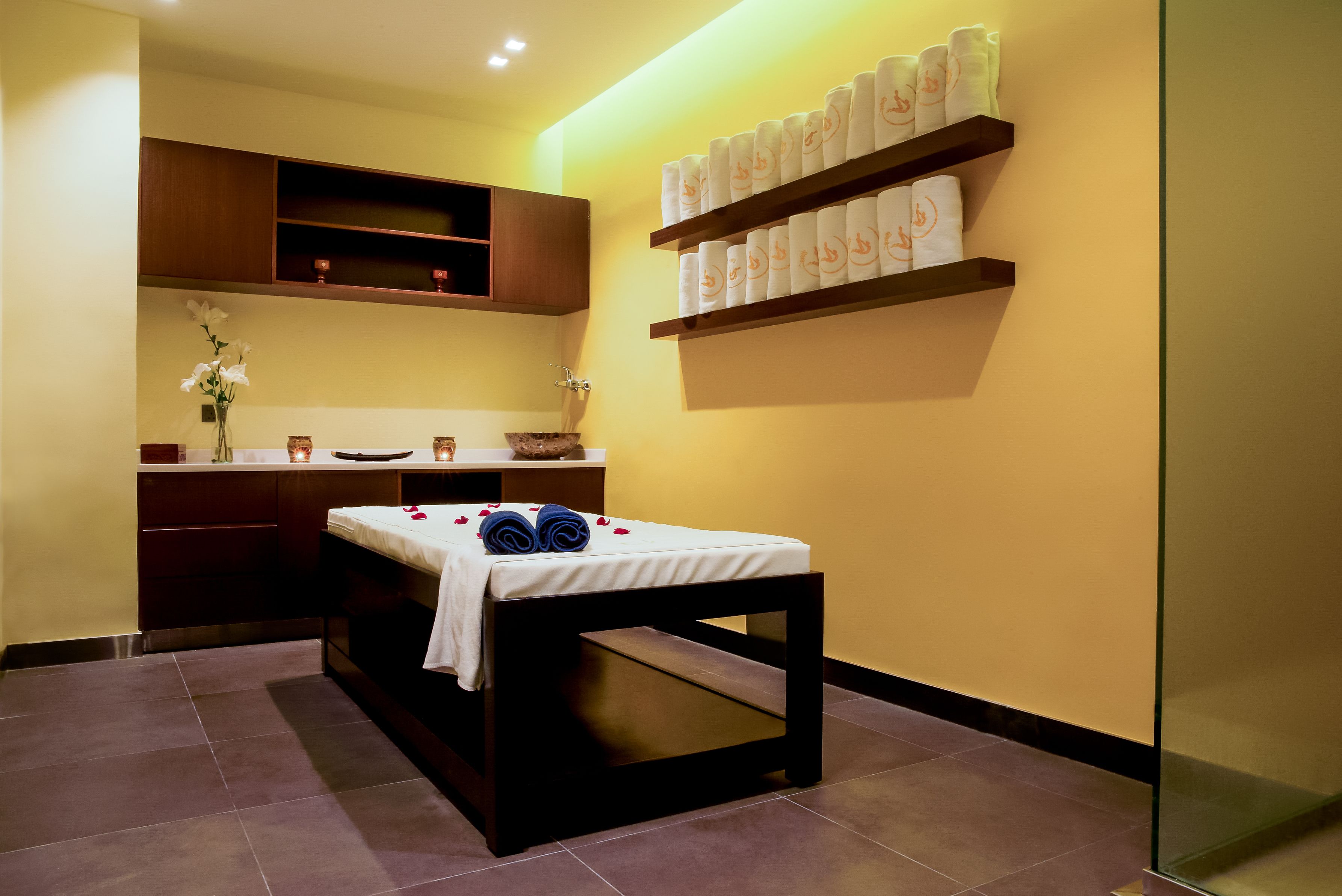 A spa room with a massage table, towels, and a shelf with towels.
