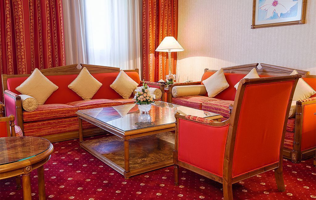 Une chambre d’hôtel avec un canapé rouge, une table basse en verre et un fauteuil rouge.
