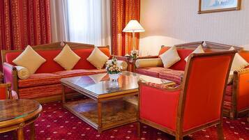 Quarto de hotel com um sofá vermelho, uma mesa de centro de vidro e uma poltrona vermelha.