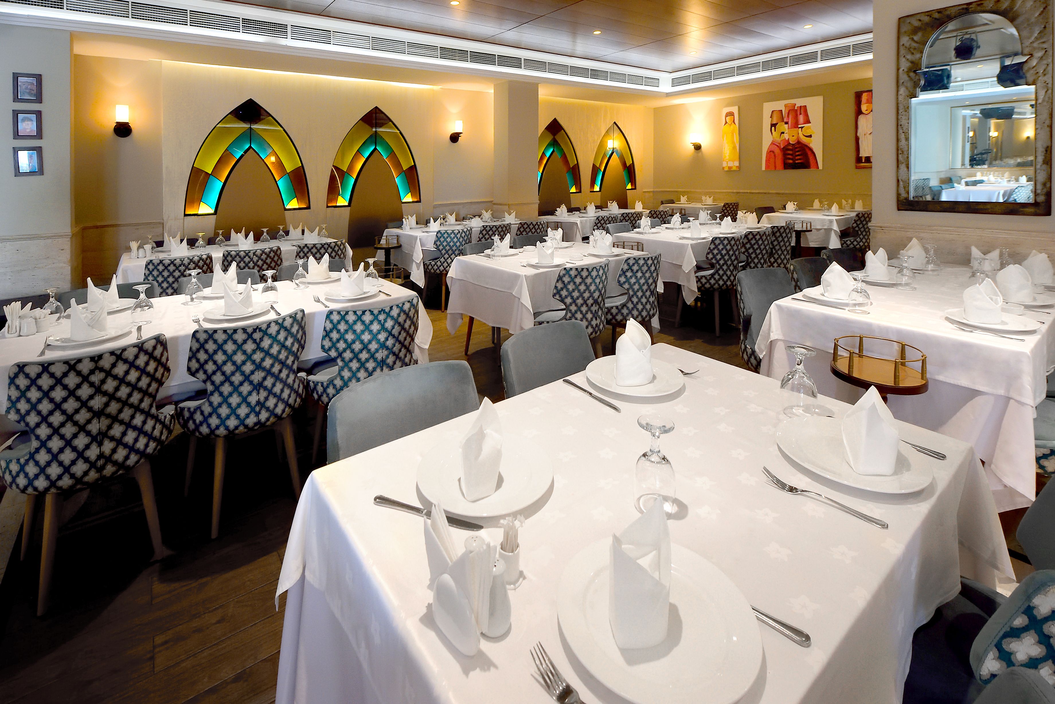 A restaurant with multiple tables set for dining, featuring patterned tablecloths and white napkins.