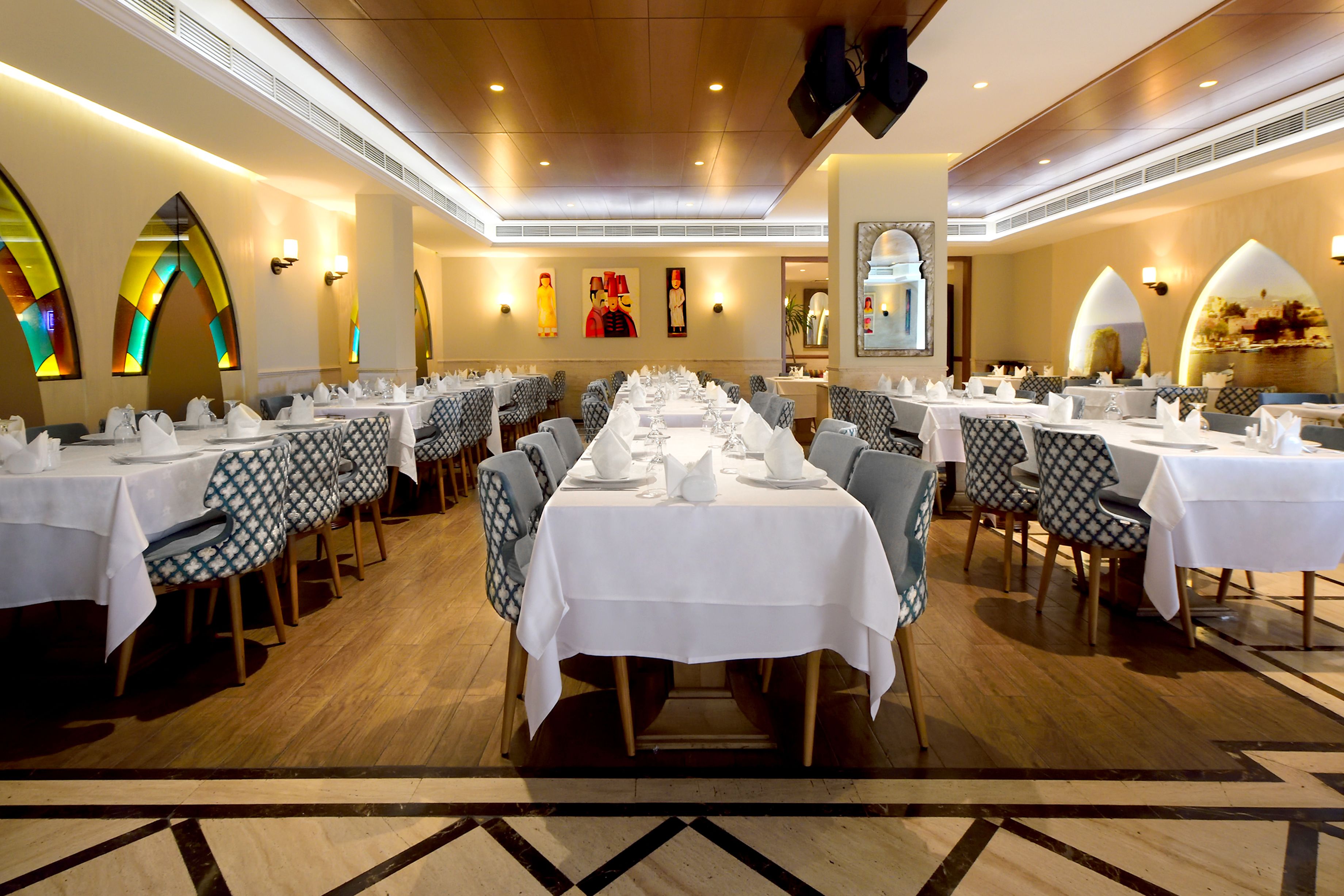 A large banquet hall with multiple tables set for dining, featuring patterned chairs and white tablecloths.