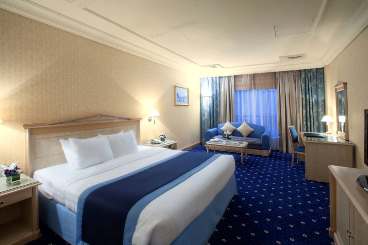 A hotel room with a large bed, a desk, a chair, and a sofa.