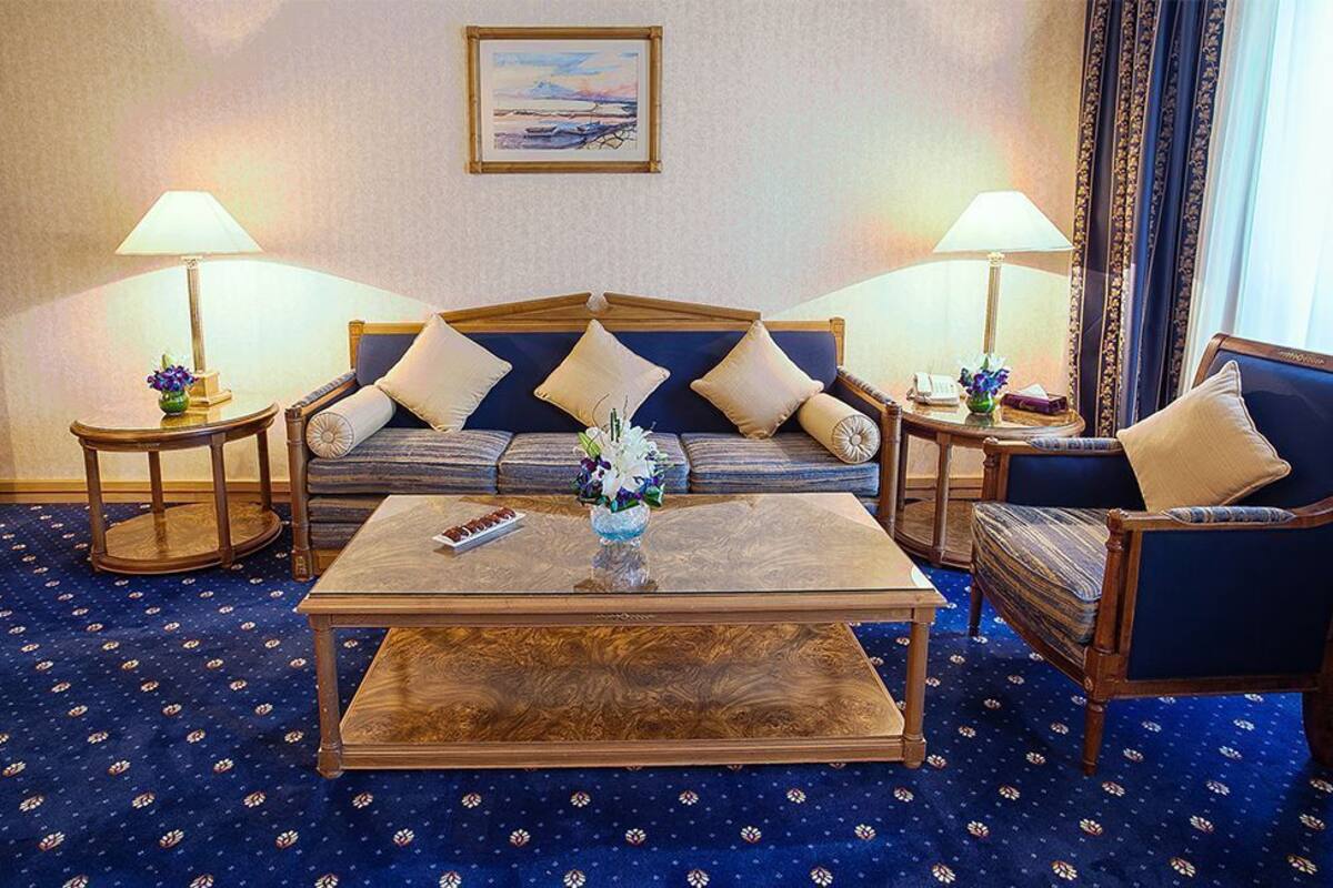 Una habitación de hotel con un conjunto de sofás, una mesa de centro, dos mesitas auxiliares con lámparas y una alfombra estampada.