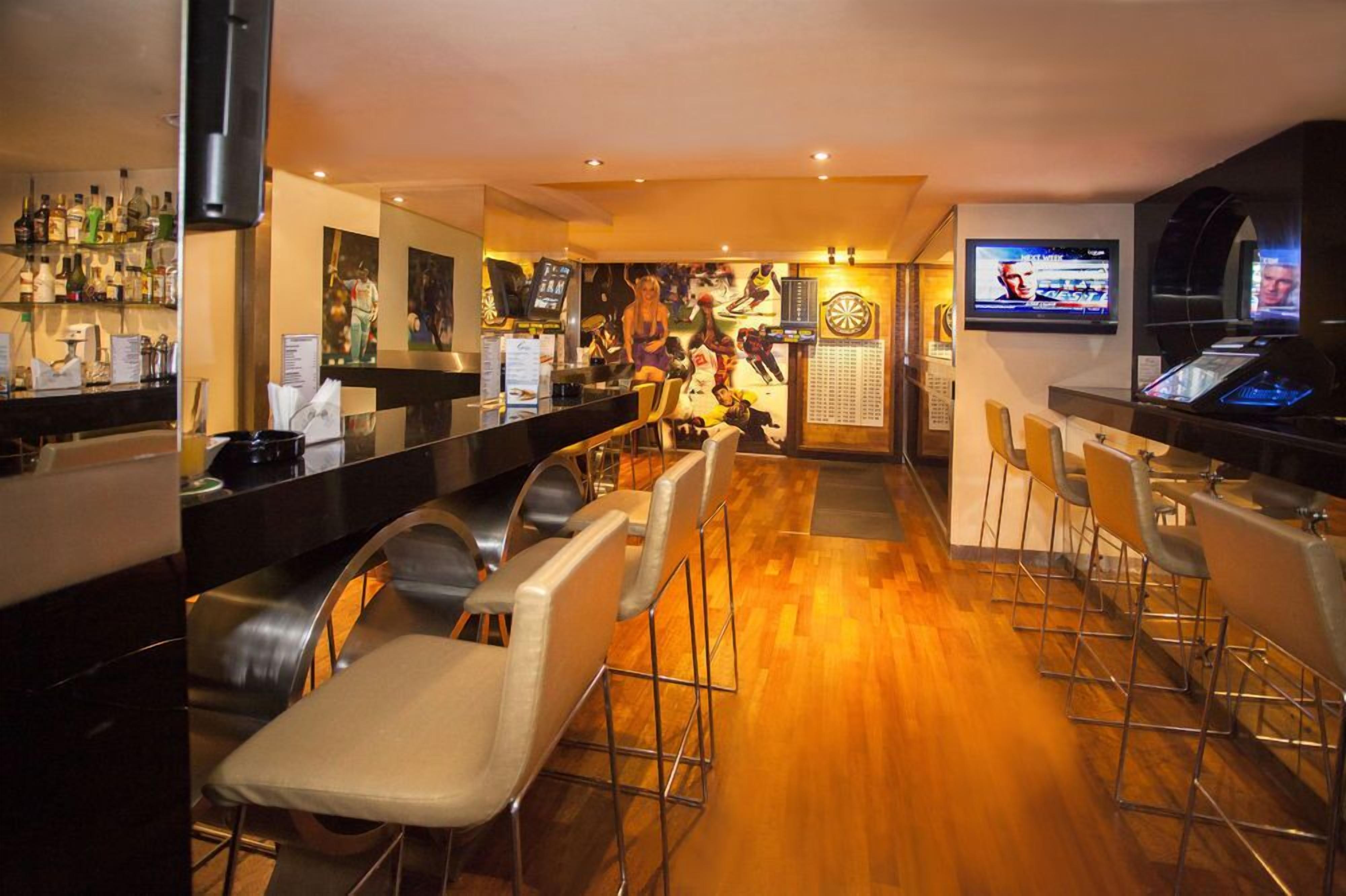 A bar area with multiple seating options, a dartboard, and a television screen displaying a sports event.
