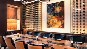 A restaurant with a long dining table, multiple wine racks, and a large abstract painting on the wall.