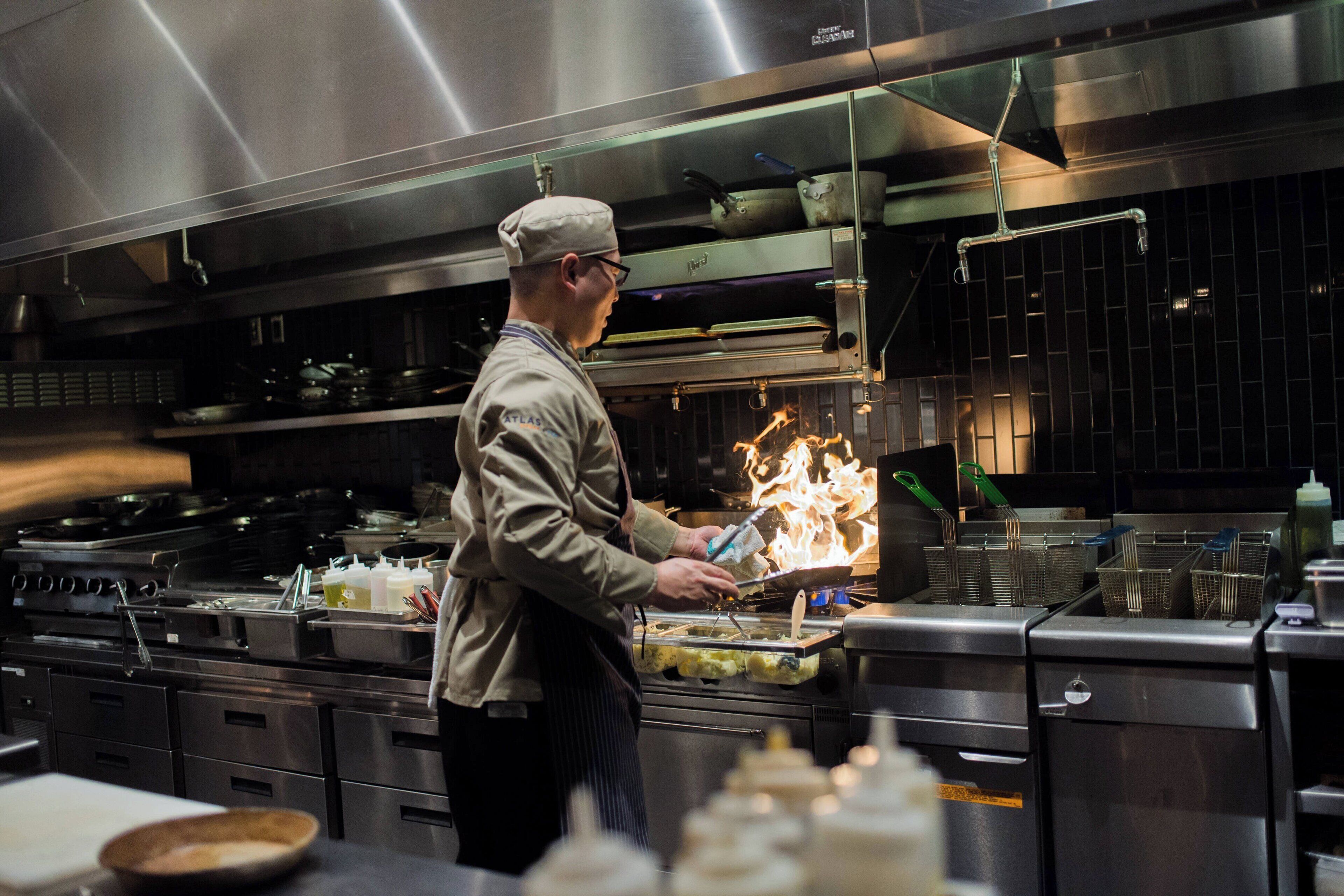 A chef working with a flame in a professional kitchen setting.