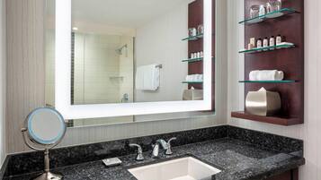 A modern bathroom with a large mirror, a granite countertop, a sink, and shelves with toiletries.
