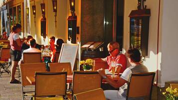 An outdoor cafe with tables and chairs, a menu board, and a person standing by the entrance.
