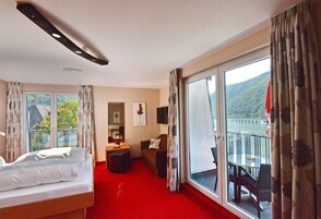 Habitación de hotel con cama, escritorio, silla, balcón con mesa y sillas, y vistas a un puente y colinas.