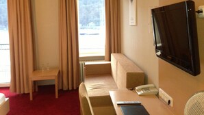 A hotel room with a bed, a desk, a chair, a television, and a window with curtains.