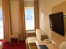 Una habitación de hotel con cama, escritorio, silla, televisor y ventana con cortinas.