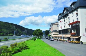A riverside hotel with outdoor seating, a view of the river, and a mountainous backdrop.
