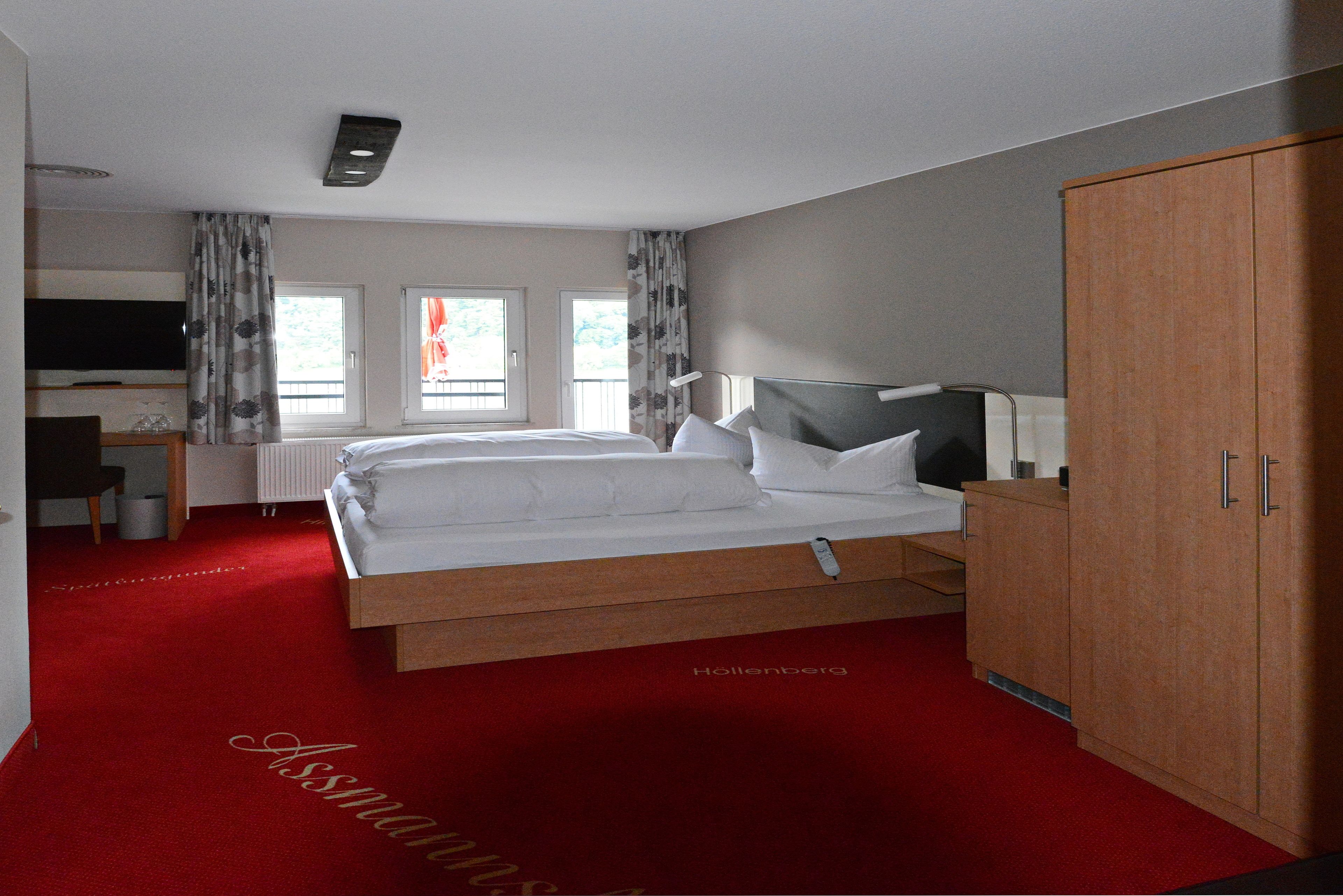 A hotel room with a large bed, a wooden wardrobe, a desk with a chair, and a television.