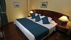 A hotel room with a large bed, two bedside lamps, a wooden headboard, and two framed pictures on the walls.