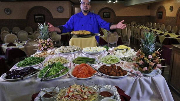 A buffet table with various food items and a chef presenting.