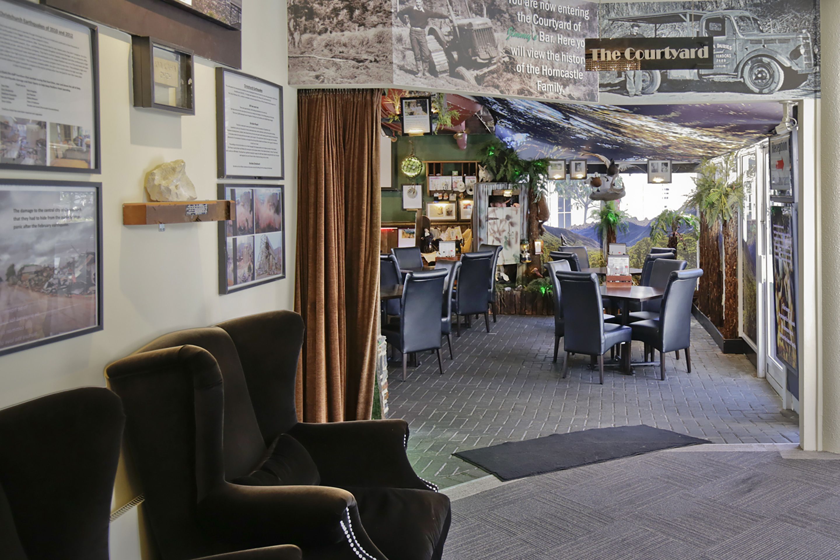 Un restaurant au décor rustique, avec des tableaux encadrés accrochés aux murs, une enseigne indiquant « La Cour » et une vue sur les montagnes par la fenêtre.