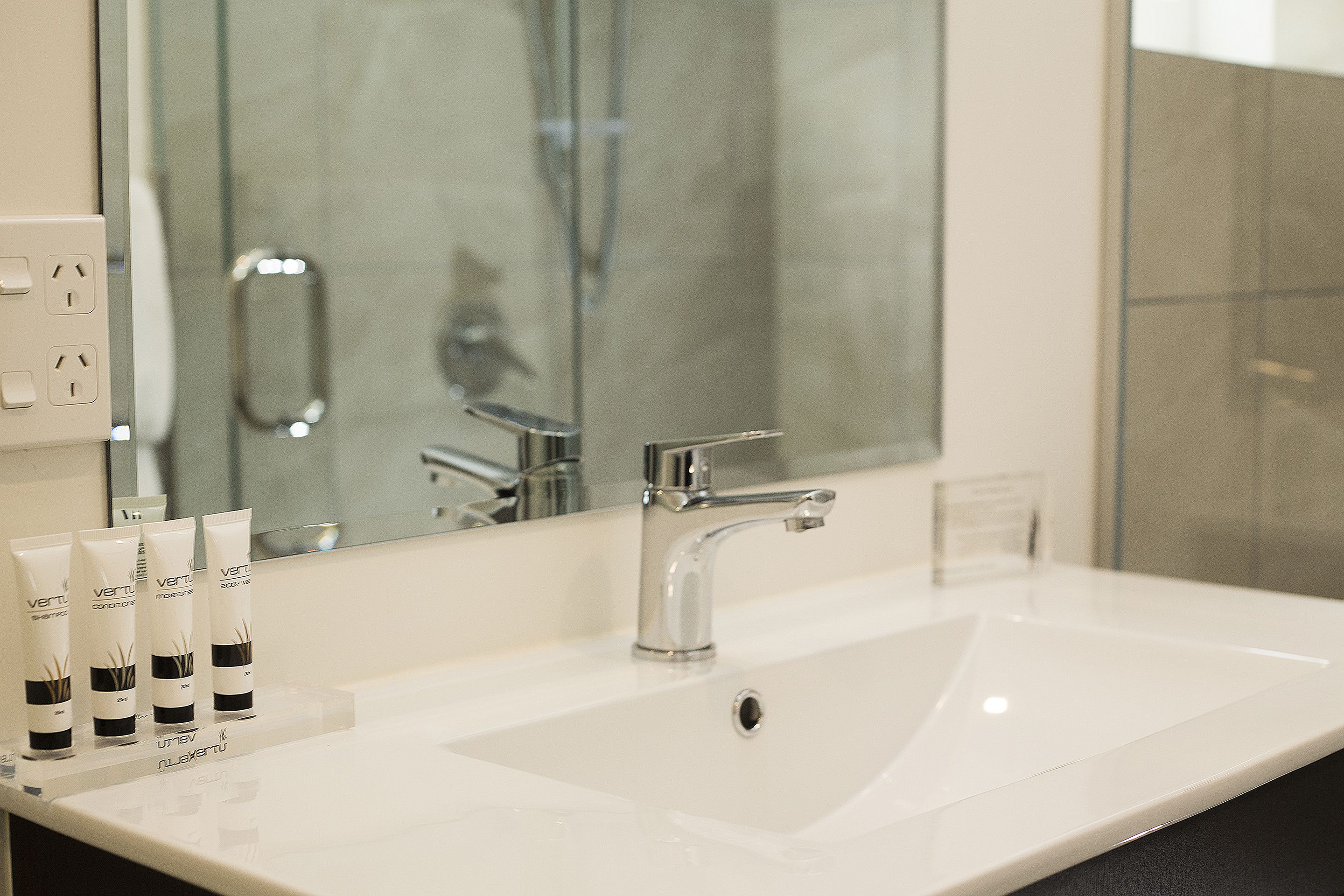 Een badkamer met een wit wastafelblad, een chromen kraan en drie tubes lotion op het aanrecht.