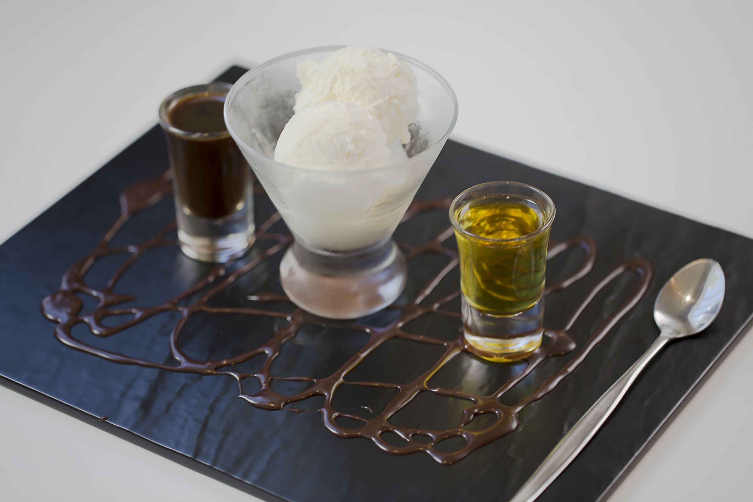 Un dessert composé de crème glacée et de sauce au chocolat, servi sur une assiette en ardoise.