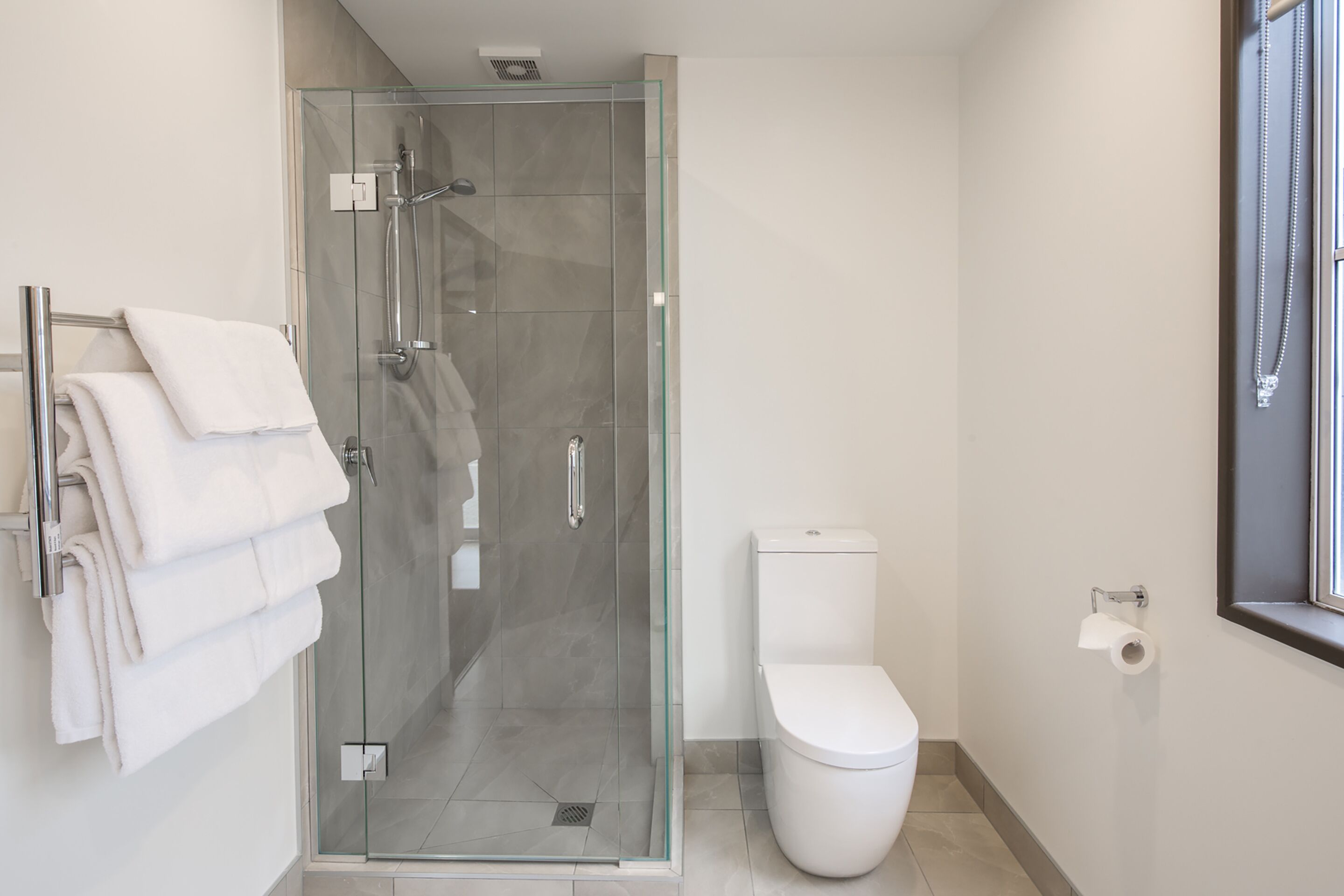 A modern bathroom with a glass-enclosed shower, a white toilet, and a towel rack with folded towels.