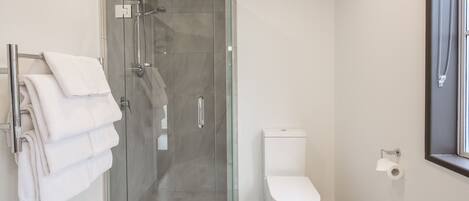 A modern bathroom with a glass-enclosed shower, a white toilet, and a towel rack with folded towels.
