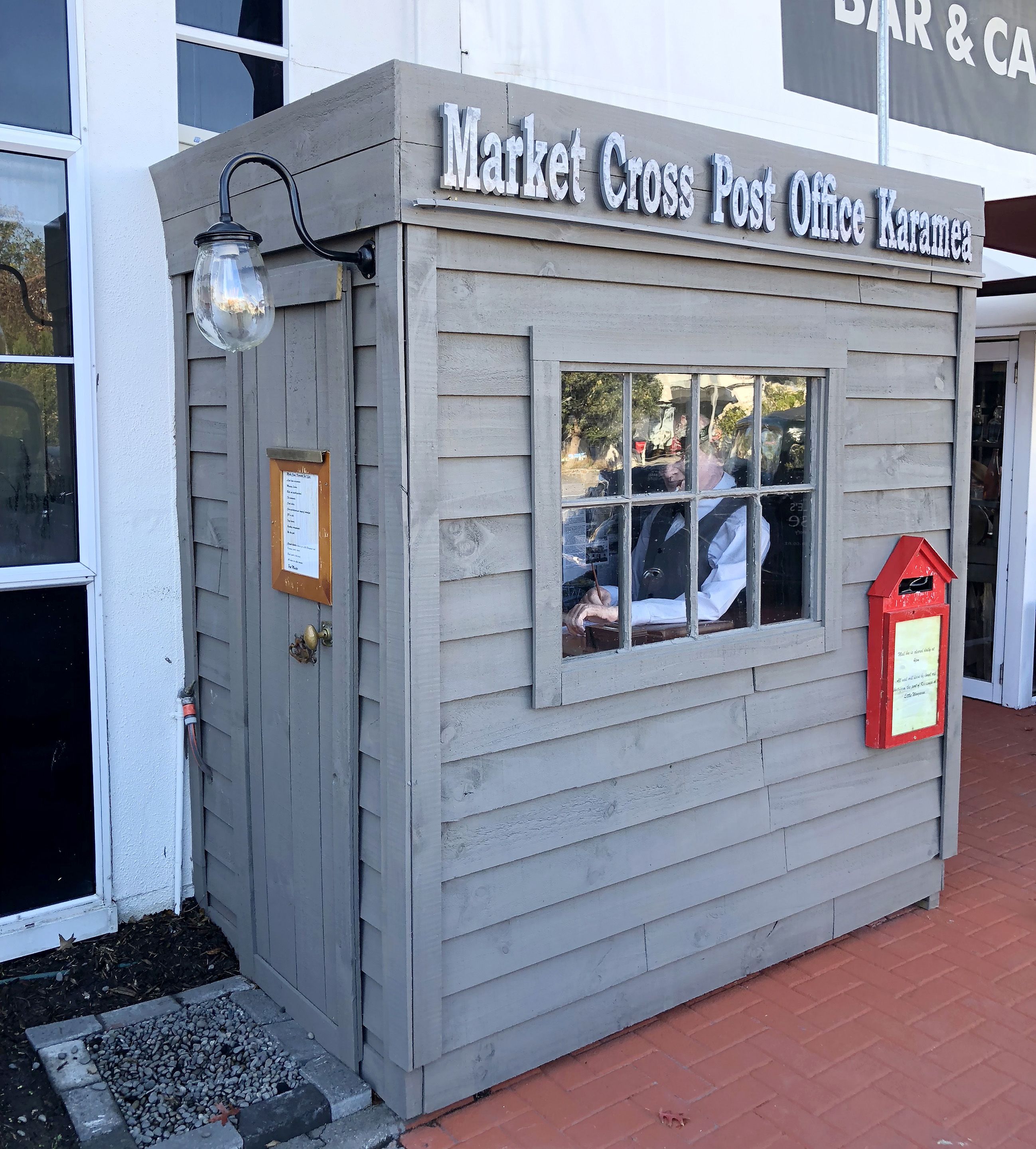 Un bureau de poste situé dans un bâtiment appelé « Market Cross », avec une façade en bois, une fenêtre et une boîte aux lettres rouge.