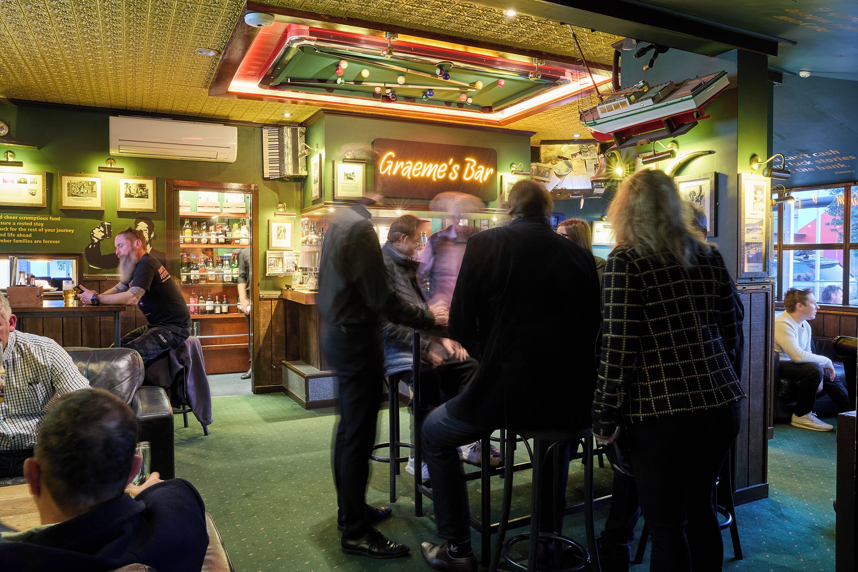 A bar with a neon sign reading "Graeme's Bar" and a pool table in the background.