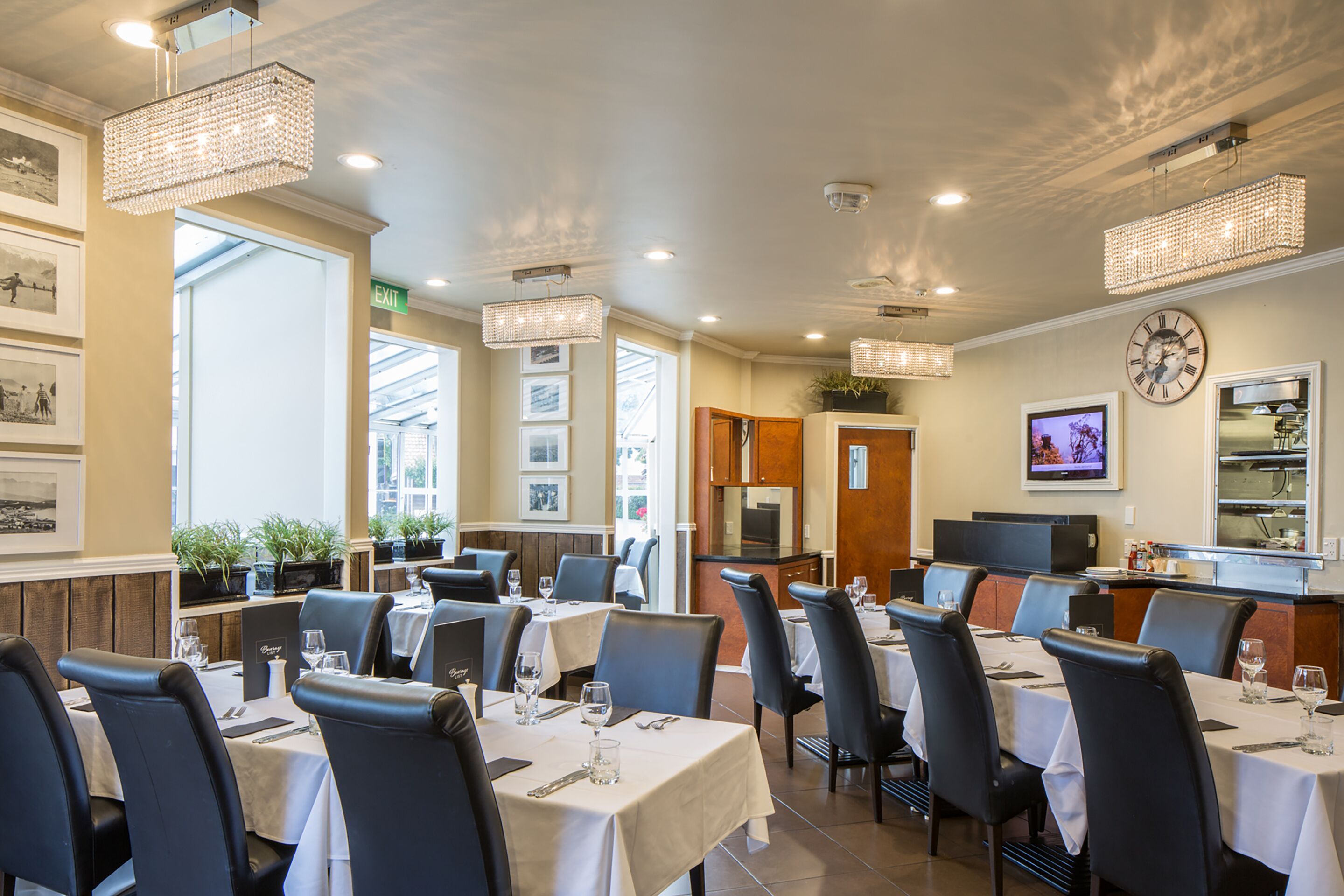 Restaurante com mesas postas para refeições, cadeiras e um relógio na parede.