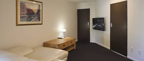 Una habitación de hotel con sofá, escritorio con lámpara, televisor y dos puertas.