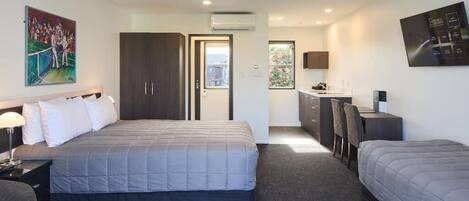 A hotel room with a bed, a desk, a chair, a wardrobe, and a painting on the wall.