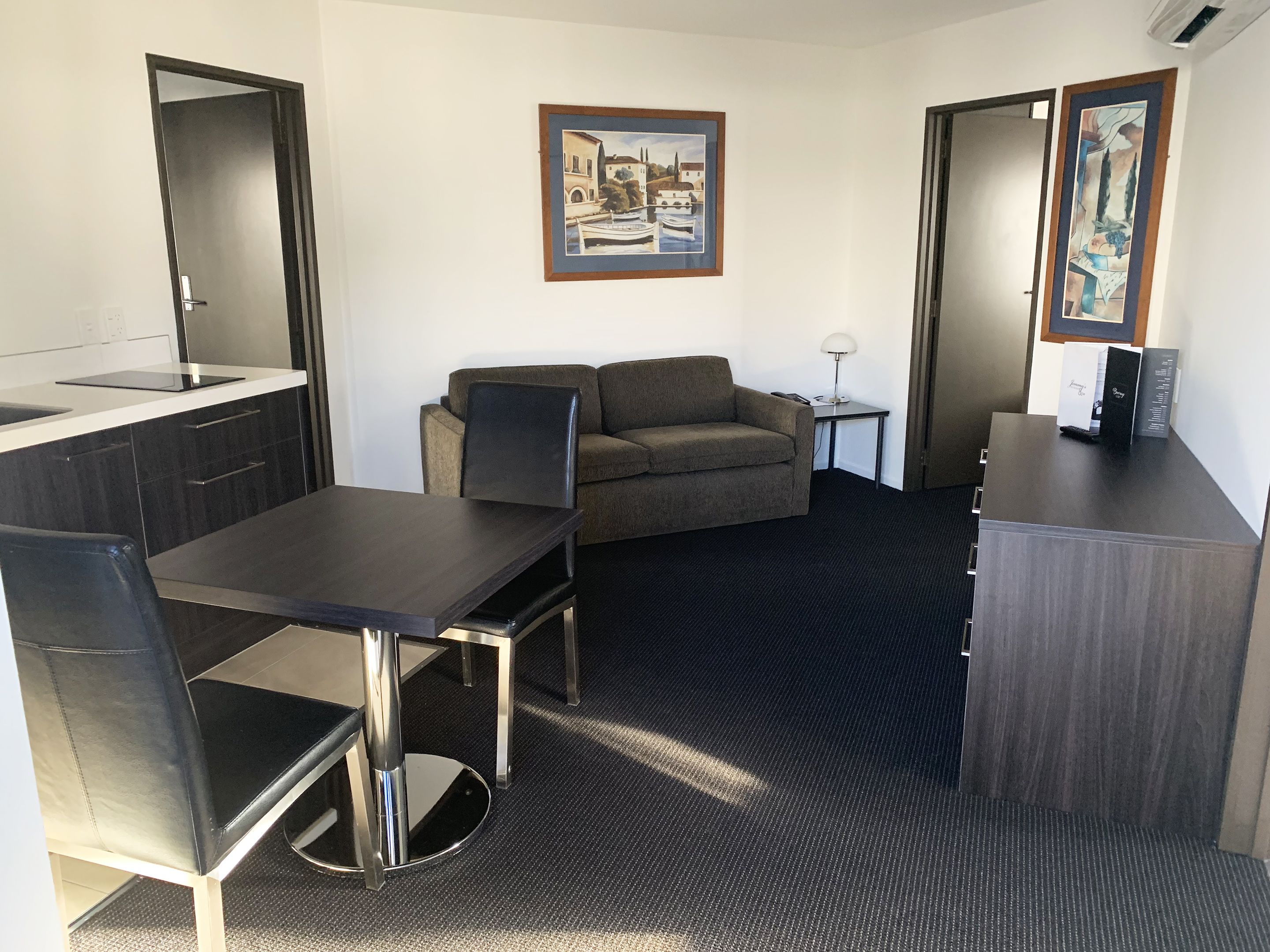 A hotel room with a kitchenette, a sofa, a dining table, and two doors.