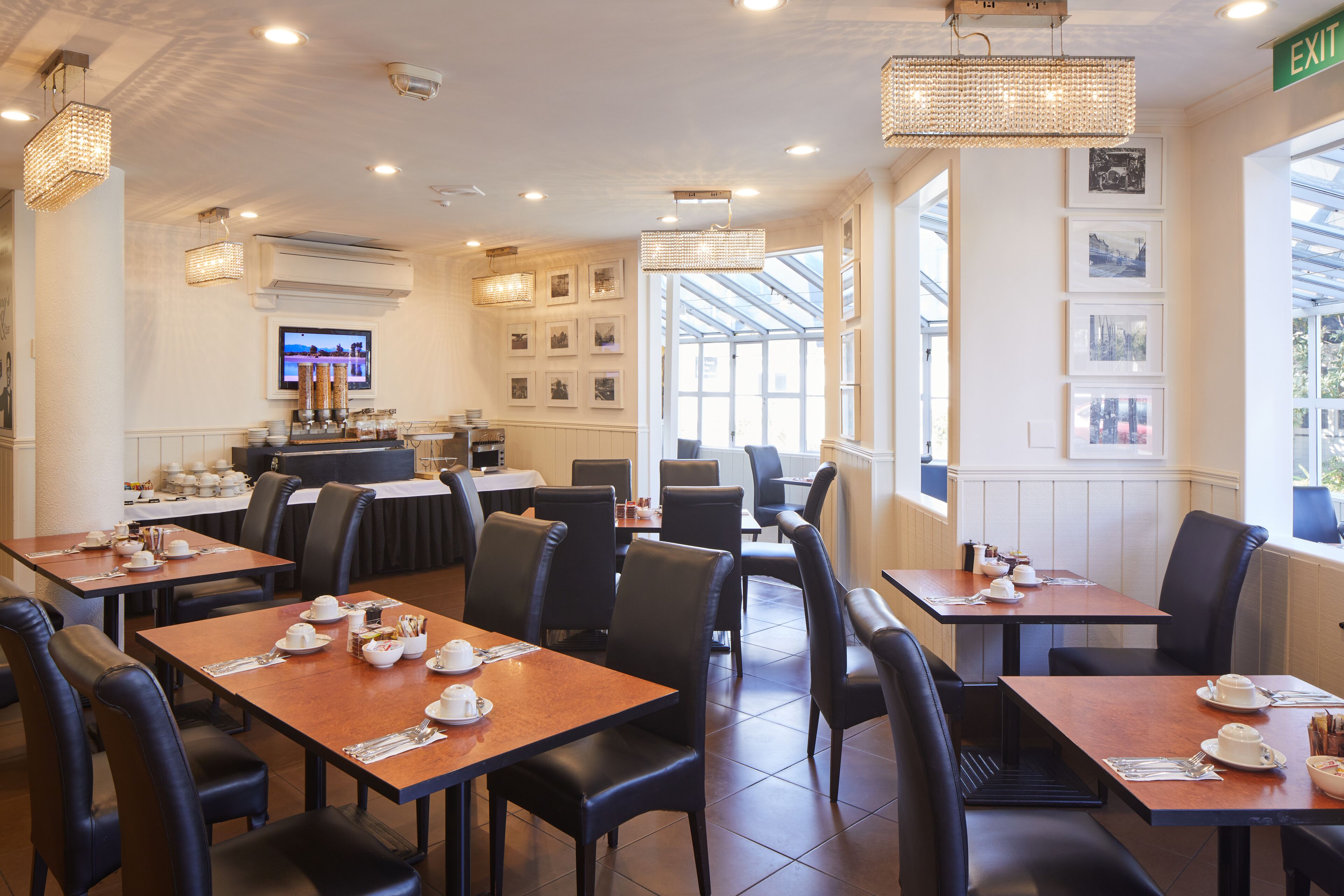 Un restaurant avec des tables dressées pour le service, un téléviseur accroché au mur et des tableaux encadrés qui décorent les murs.