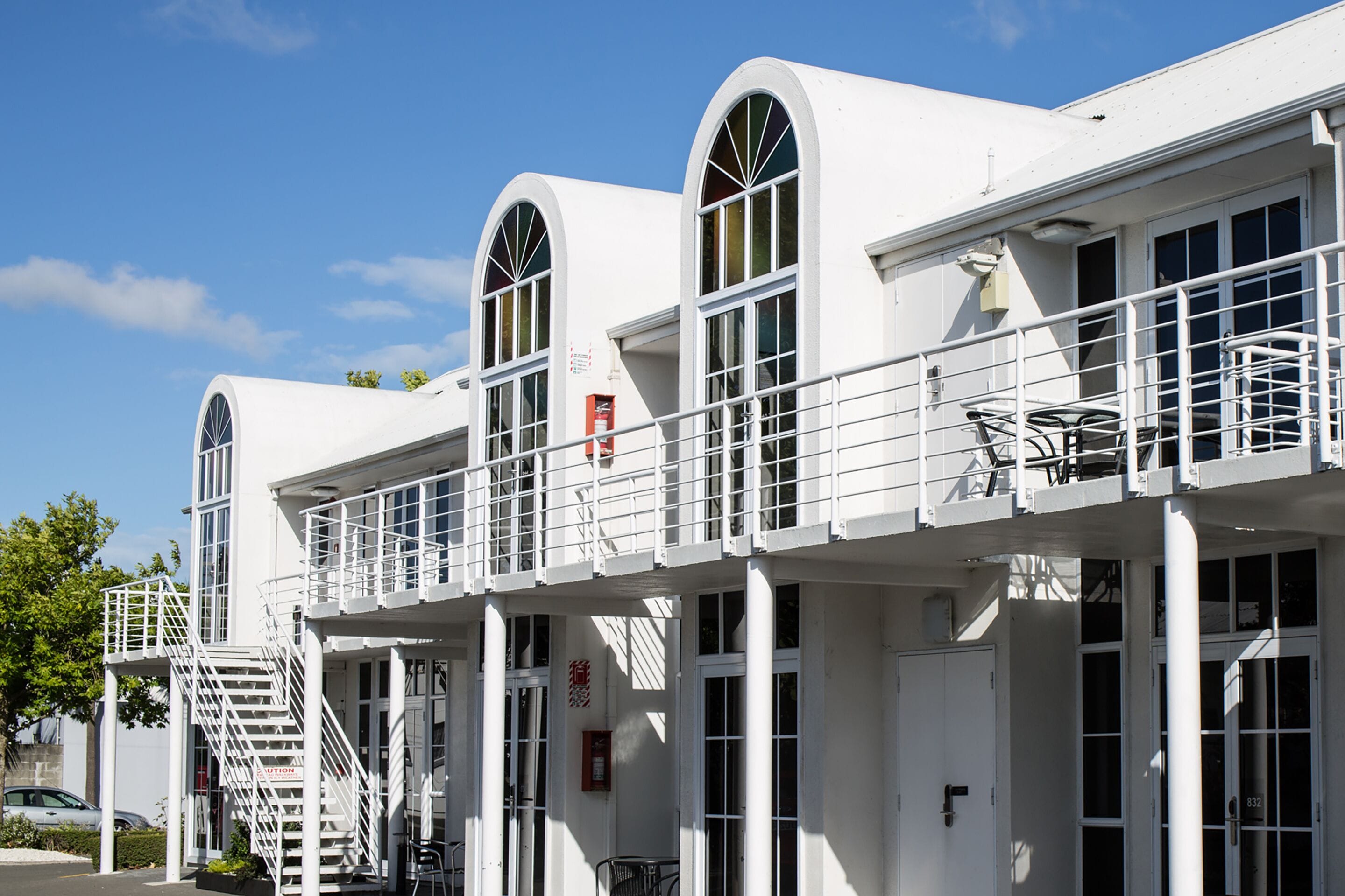 A row of white buildings with arched windows and balconies, featuring a staircase and a bike rack.