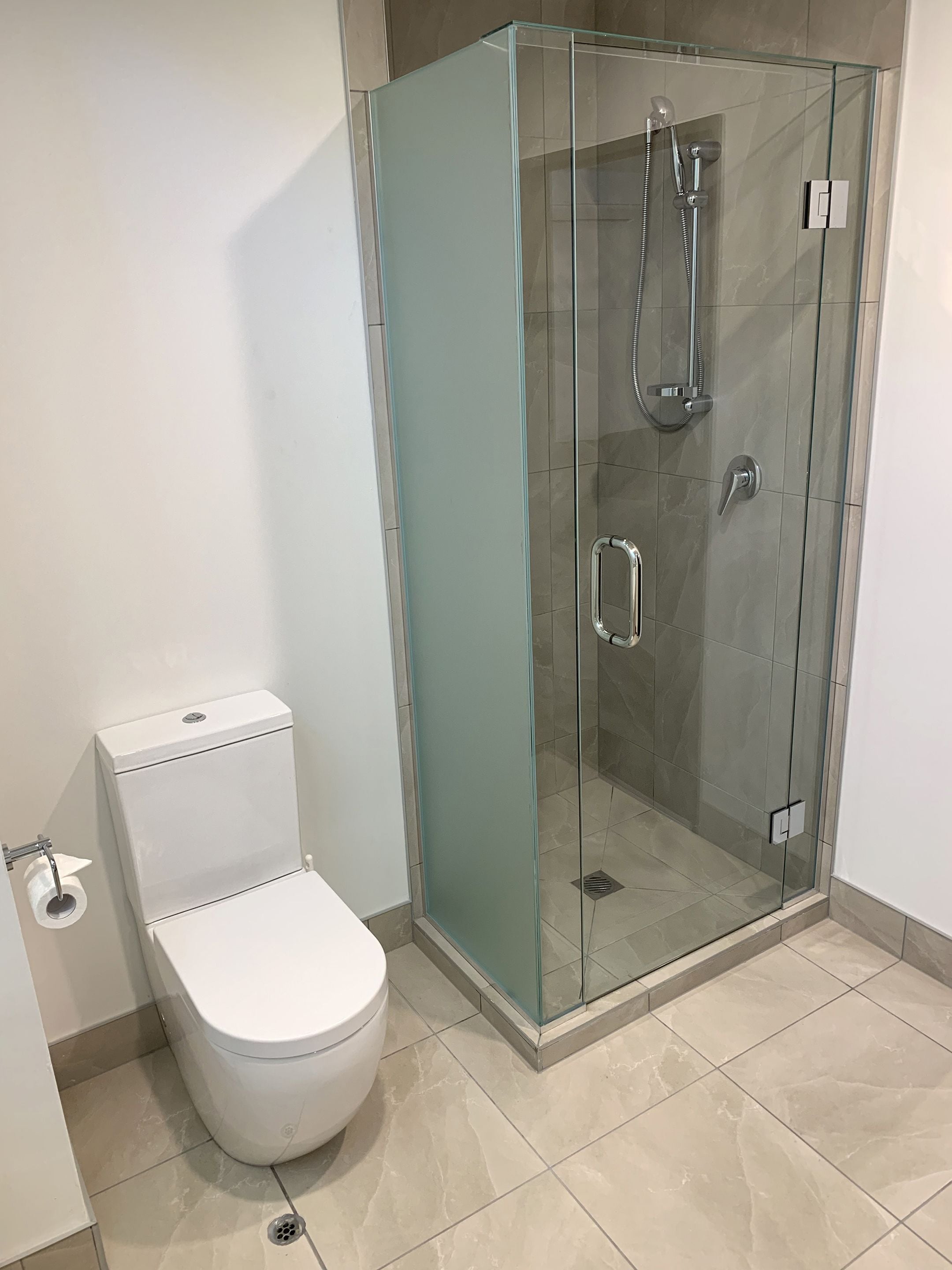 Un baño con ducha envuelta en vidrio, inodoro blanco y suelo de baldosas.